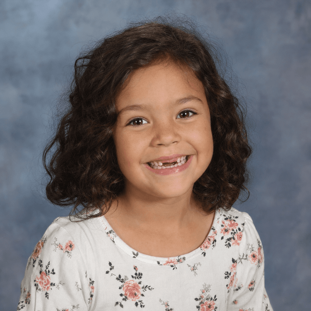 A school picture-day photo of a smiling girl with curly brown hair